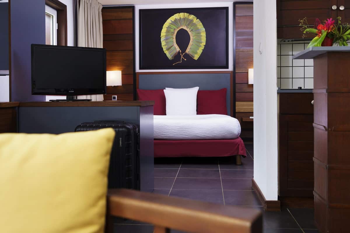 Habitación de hotel con cama, escritorio con televisor, silla y un adorno en la pared.