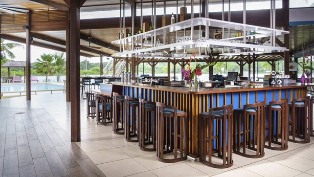 Zona de bar con vista a la piscina, taburetes de madera y suelo de baldosas.