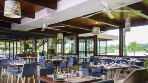 Un restaurante con varias mesas y sillas, ventanas amplias, ventiladores de techo e iluminación colgante.