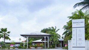 La entrada del Hotel Mercure con un área de espera cubierta, una señalización con indicaciones y un estacionamiento.