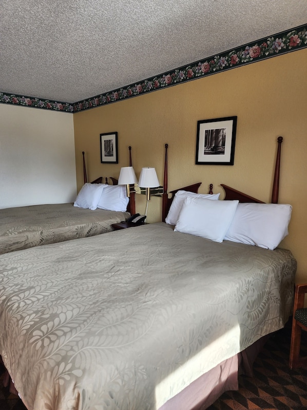 Une chambre d’hôtel avec deux lits, une table de chevet avec une lampe et des tableaux encadrés au mur.