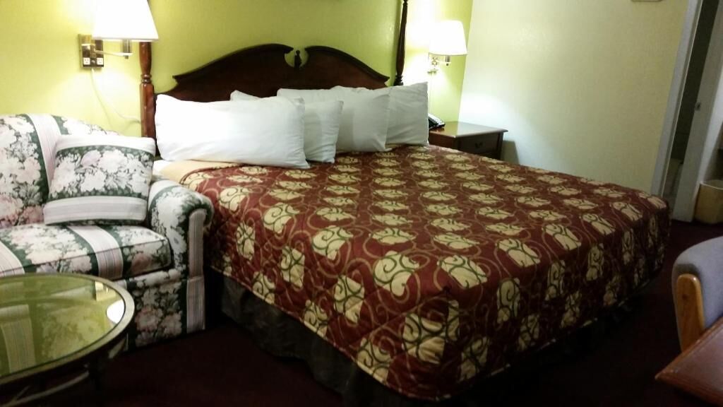 A hotel room with a bed, a floral armchair, a small table, and two bedside lamps.