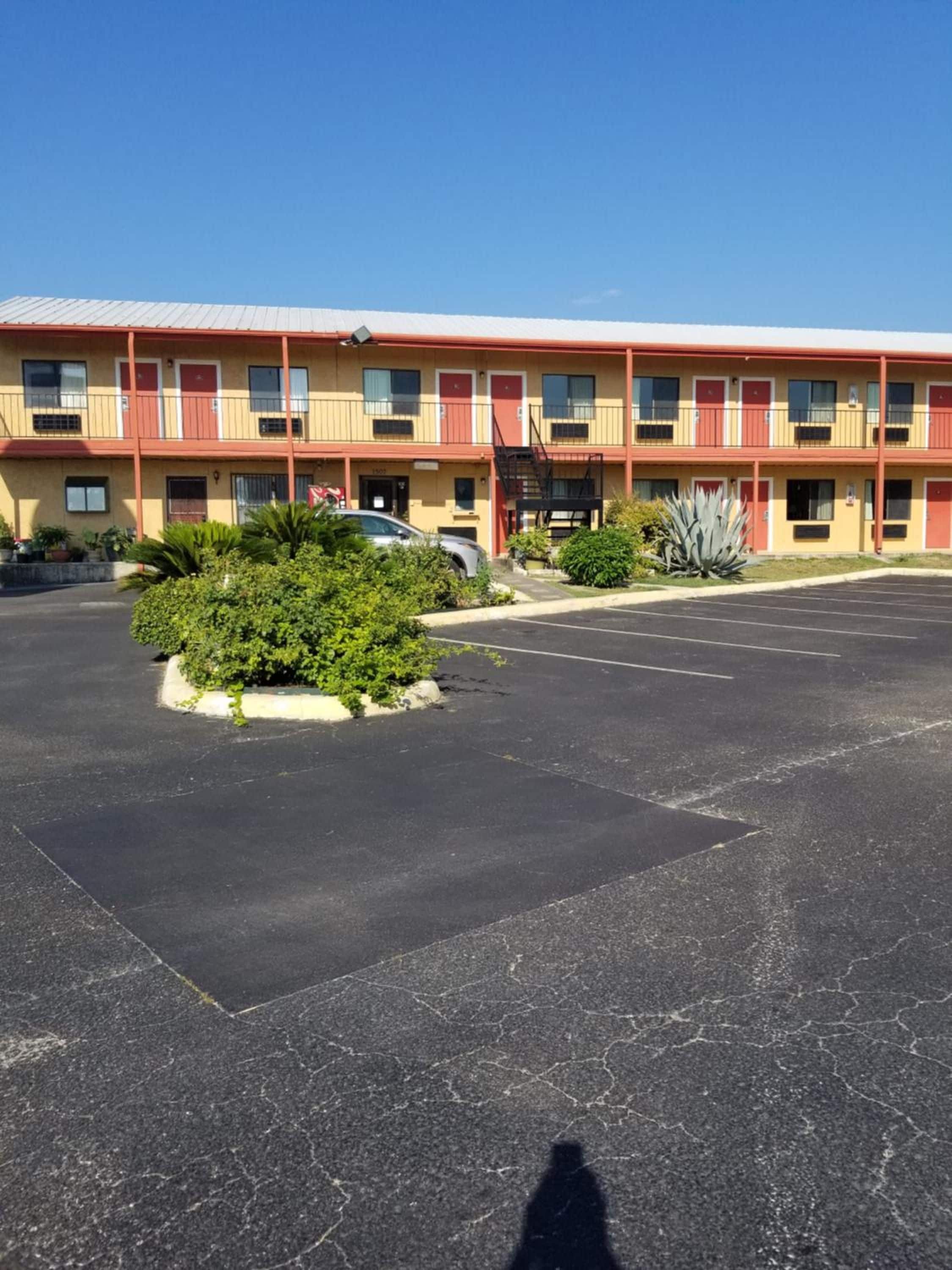 A multi-story motel with a parking lot, a fire escape, and a small landscaped area with plants.