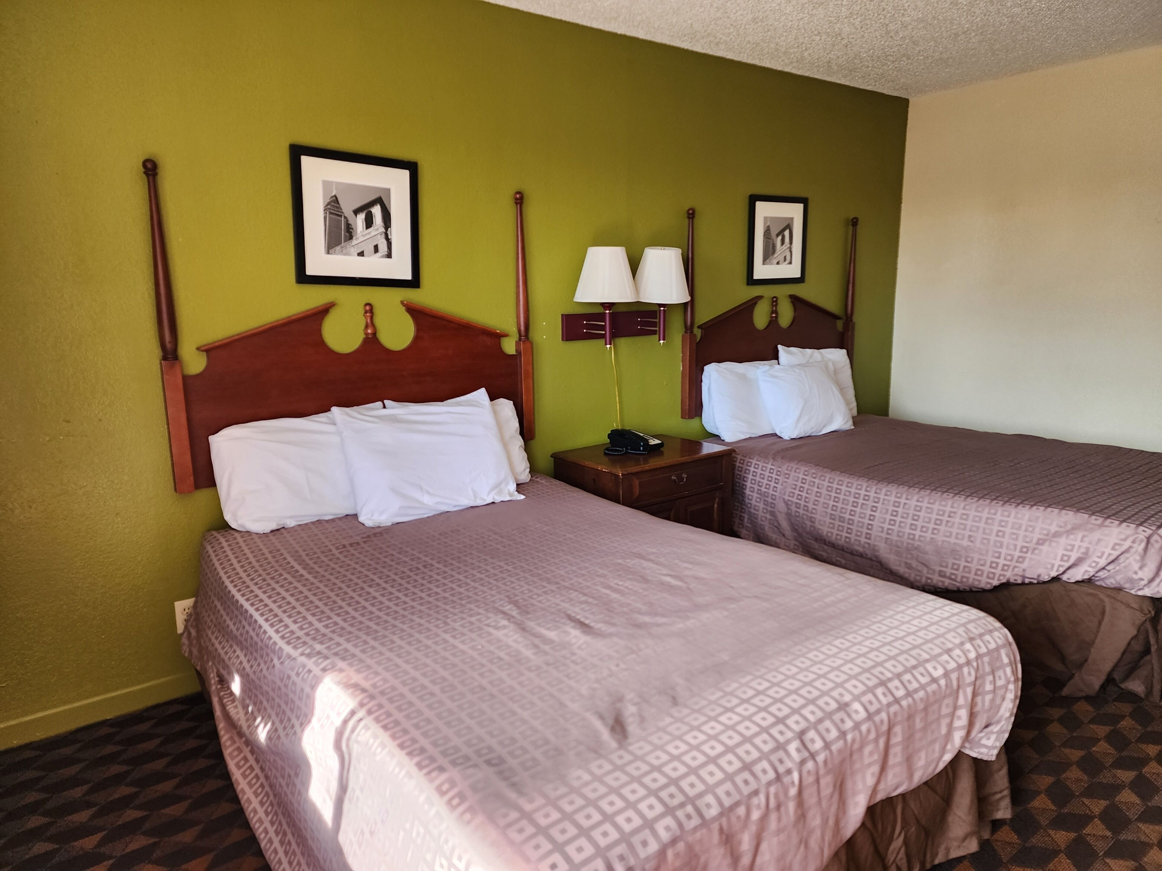 A hotel room with two beds, each with a wooden headboard, a nightstand with a lamp, and a wall-mounted picture.