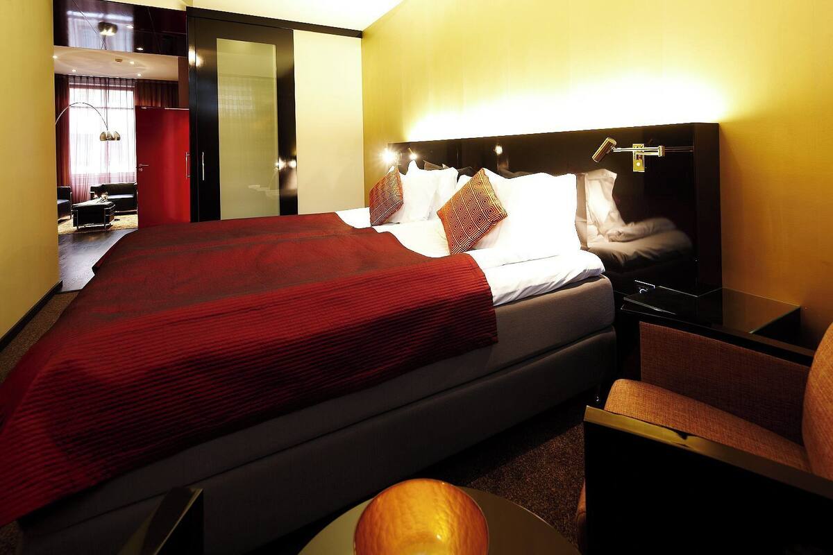 Ett hotellrum med en stor säng, ett nattduksbord, en stol och ett skrivbord med en lampa.