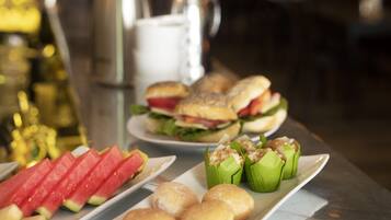 Una mesa de buffet con diferentes opciones de comida, incluyendo rebanadas de sandía, sándwiches y pasteles.