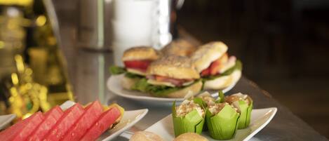 A buffet table with various food items including watermelon slices, sandwiches, and pastries.