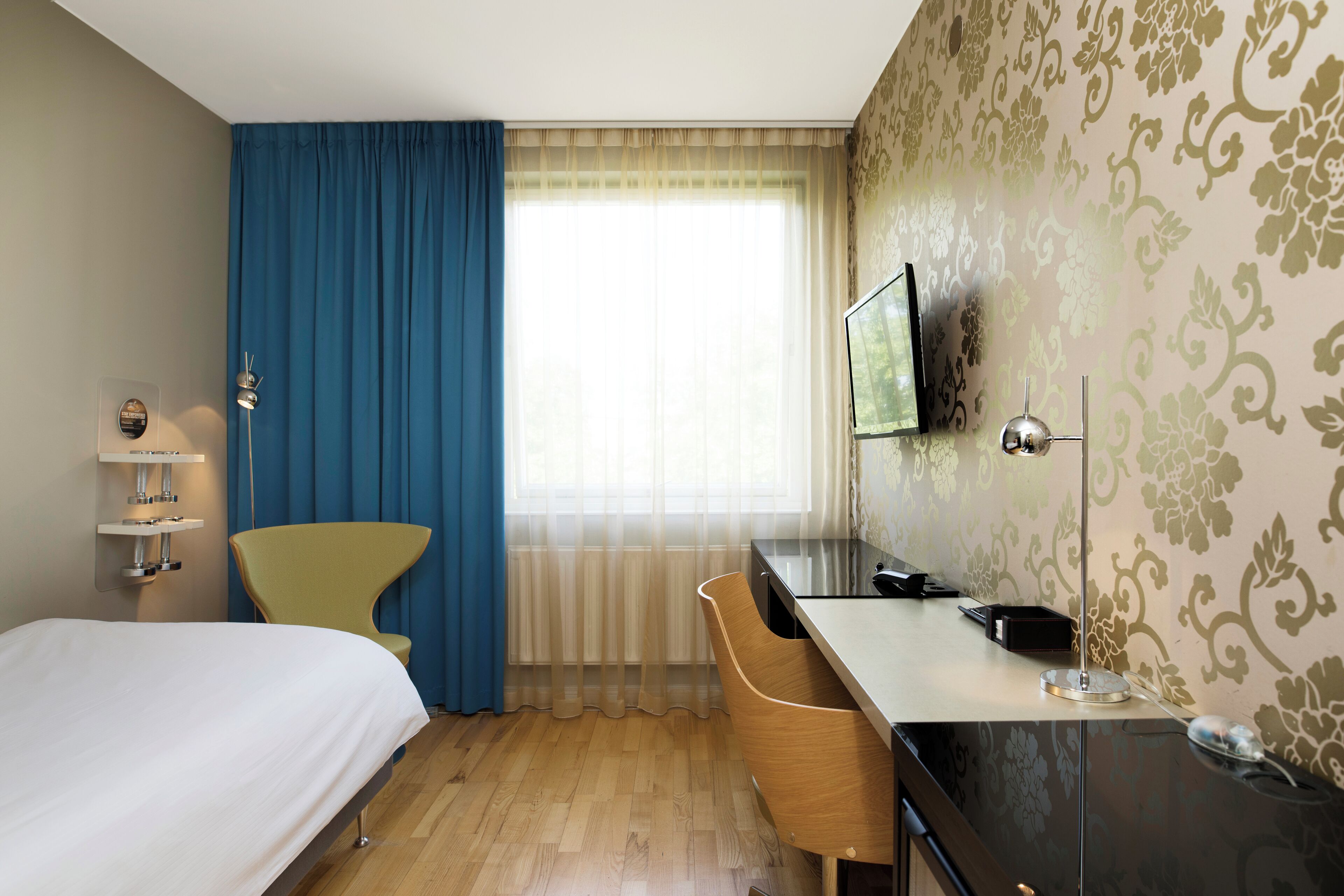 A hotel room with a bed, a desk, a chair, a television, and a window with curtains.