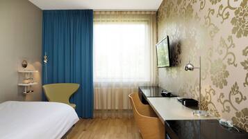 A hotel room with a bed, a desk, a chair, a television, and a window with curtains.