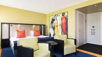 A hotel room with a bed, two chairs, a small table, a painting, and a door.
