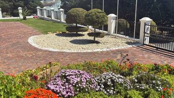 Un jardin aménagé avec un sentier en briques, un espace circulaire recouvert de gravier et diverses plantes à fleurs.