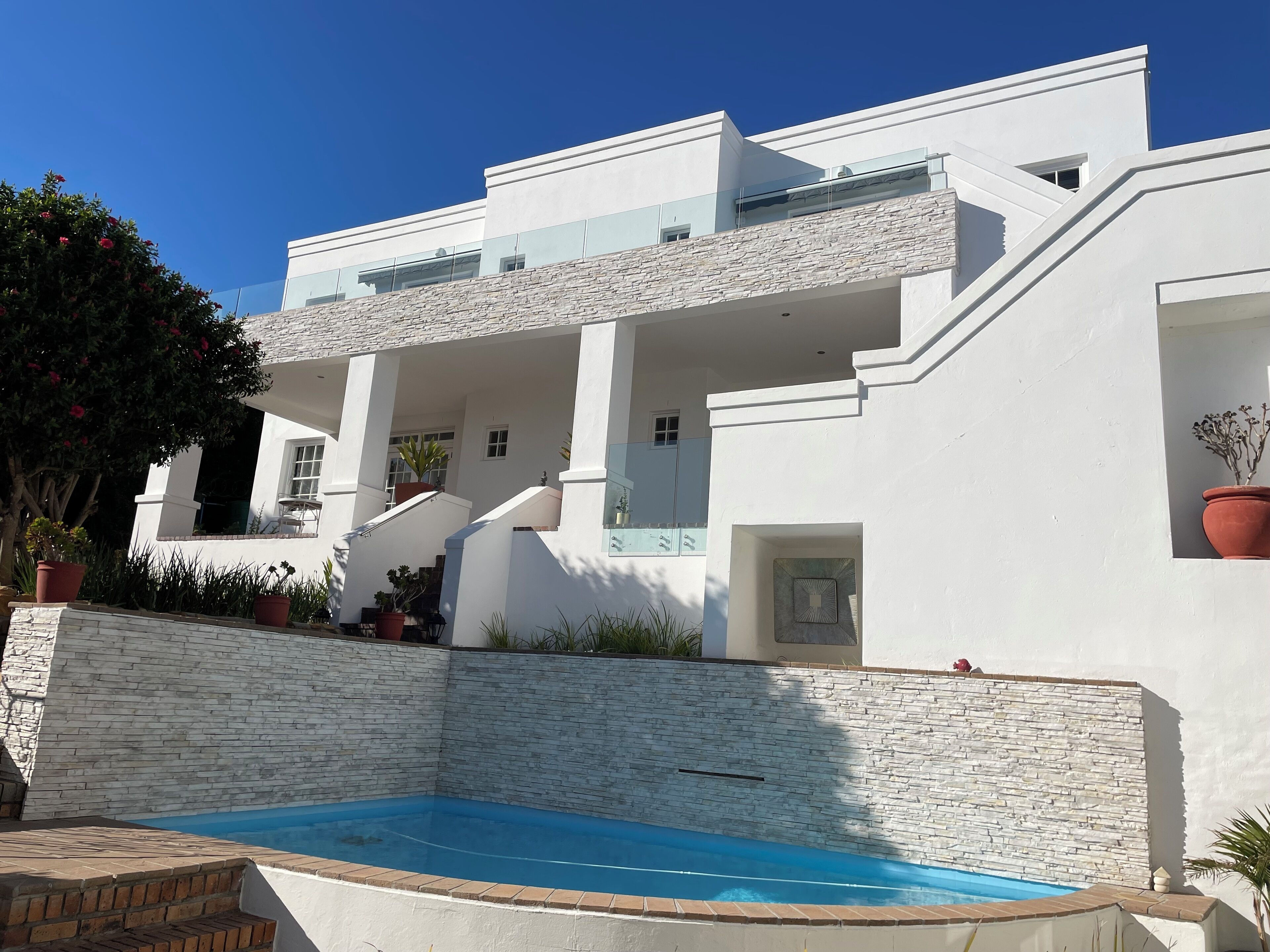 A modern white building with a stone wall and a swimming pool.