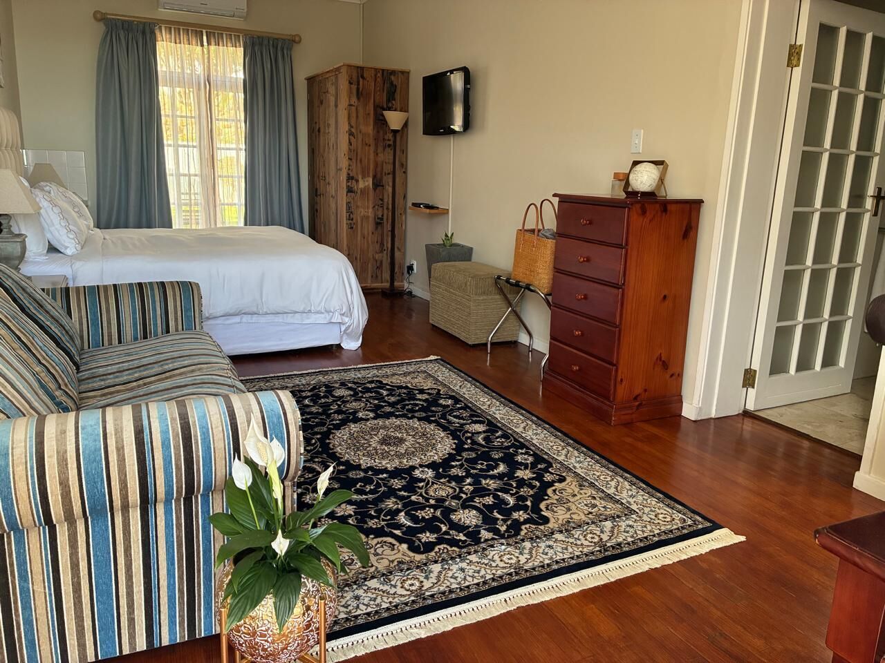 A bedroom with a bed, a striped sofa, a wooden wardrobe, a TV, and a large rug.