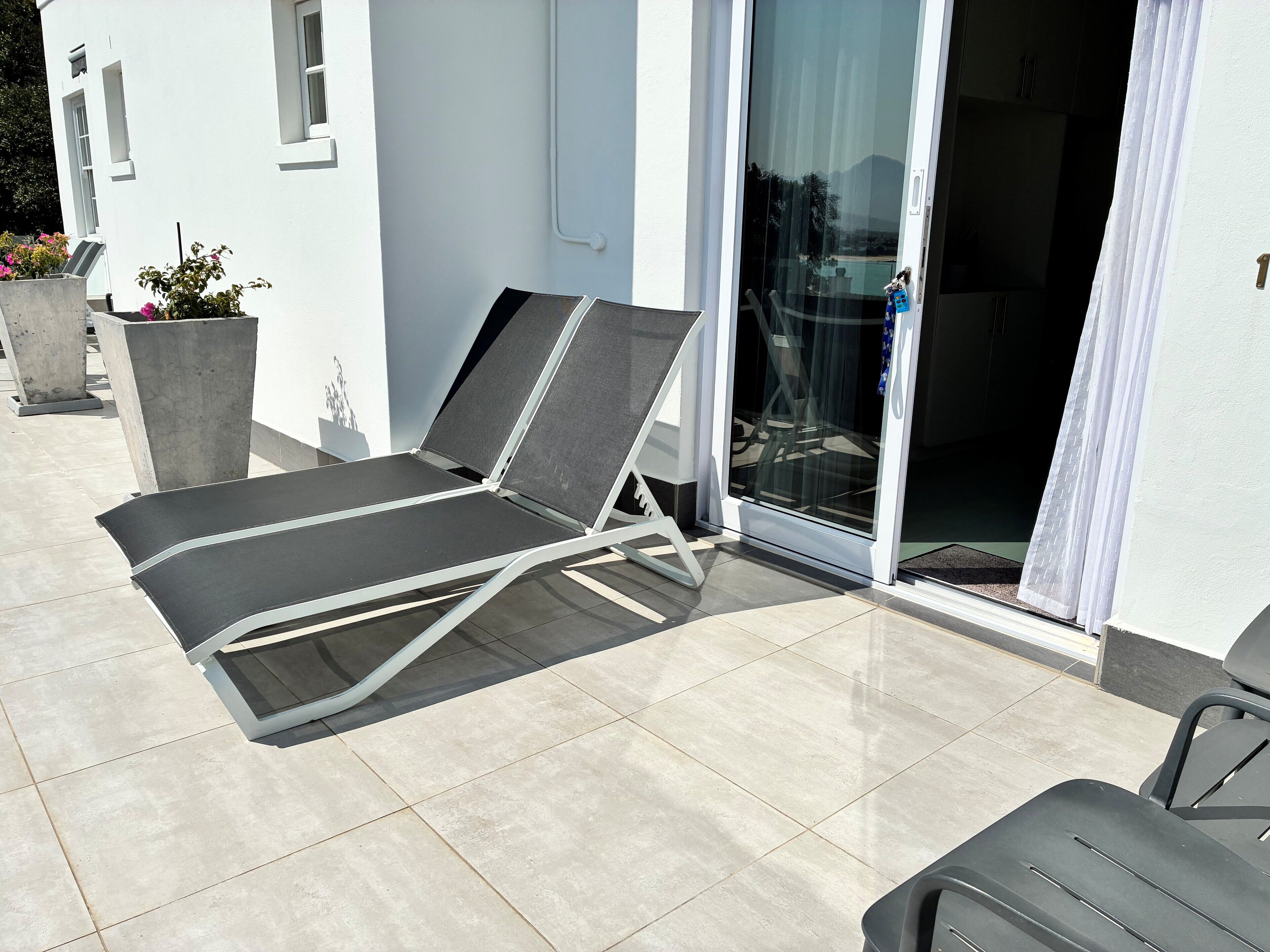 Un espace de détente extérieur moderne, comprenant un seul fauteuil inclinable, une porte vitrée donnant accès à une piscine et un sol carrelé.