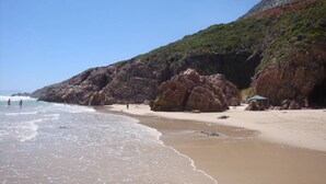 A beach with rocky cliffs, clear skies, and a few people.