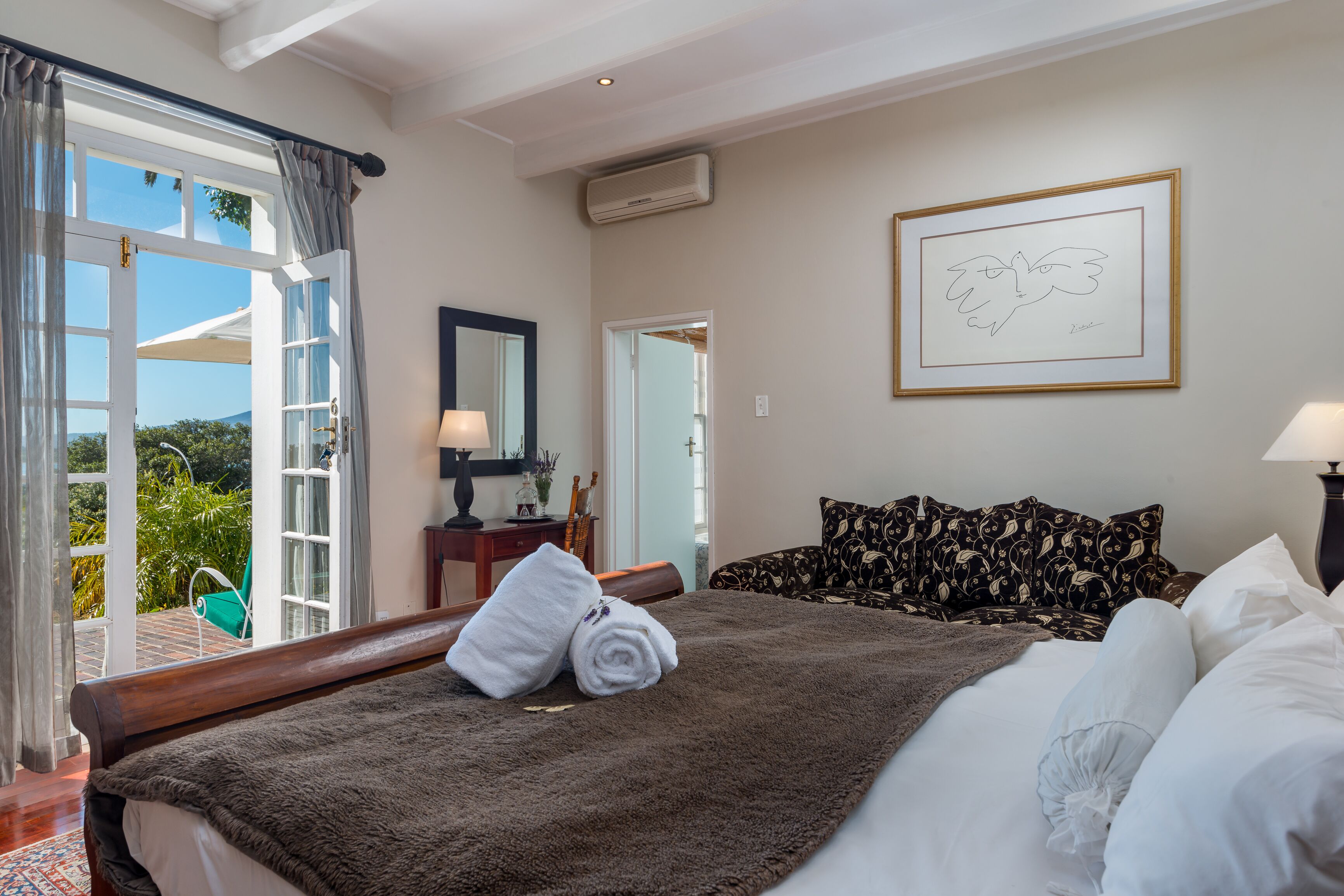 Habitación de hotel con una cama grande, vista a través de una puerta abierta, una obra de arte enmarcada en la pared y una ventana con cortinas.