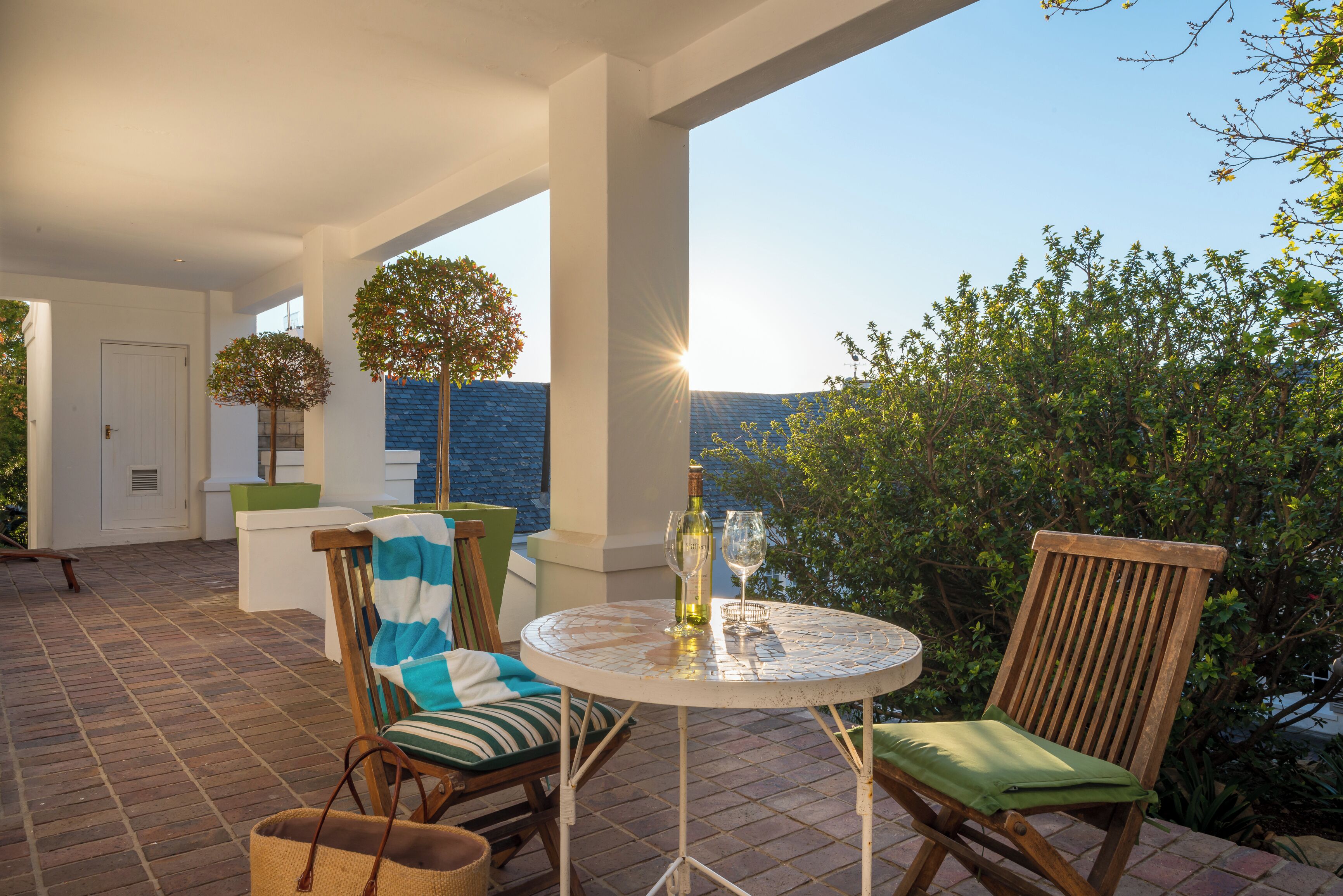 An outdoor patio with a round table, two chairs, a bottle, and glasses.