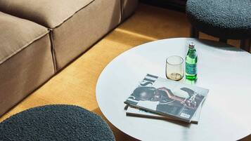 A modern living room with a beige sofa, two dark chairs, a round white table with a magazine, a glass, and a bottle.