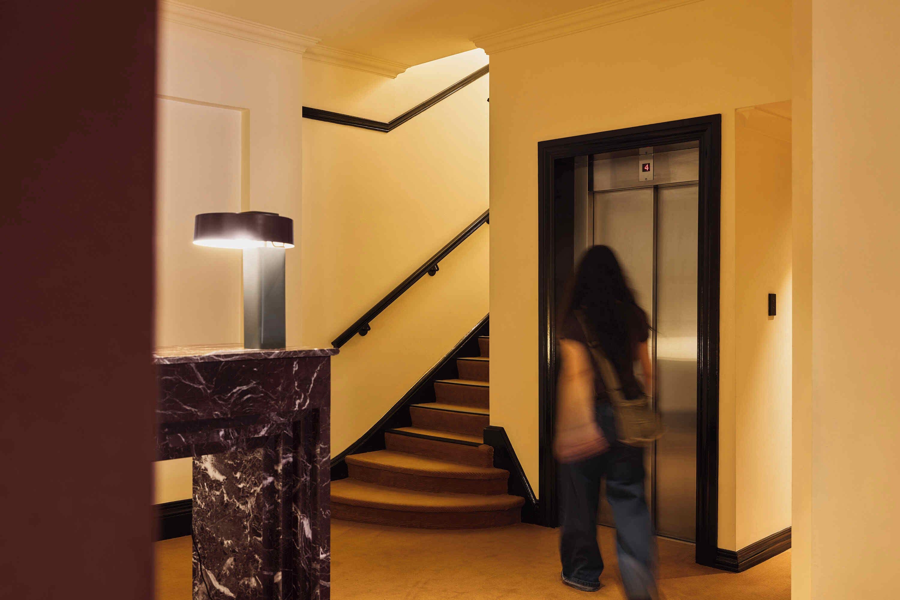 A marble staircase with a black handrail leading to an elevator.