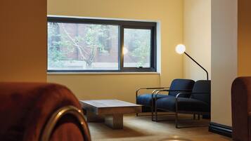 A room with a large window, a bench, two chairs, and a floor lamp.