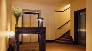 Une table en marbre surmontée d’un vase de fleurs, un luminaire fixé au mur et un escalier muni d’une main courante.