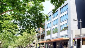 Un bâtiment moderne à étages, doté de grandes fenêtres et d’un café situé au rez-de-chaussée.