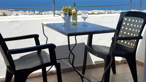 A balcony with a table and two chairs, overlooking a coastal cityscape. - Amazones Village Suites (Hersonissos)