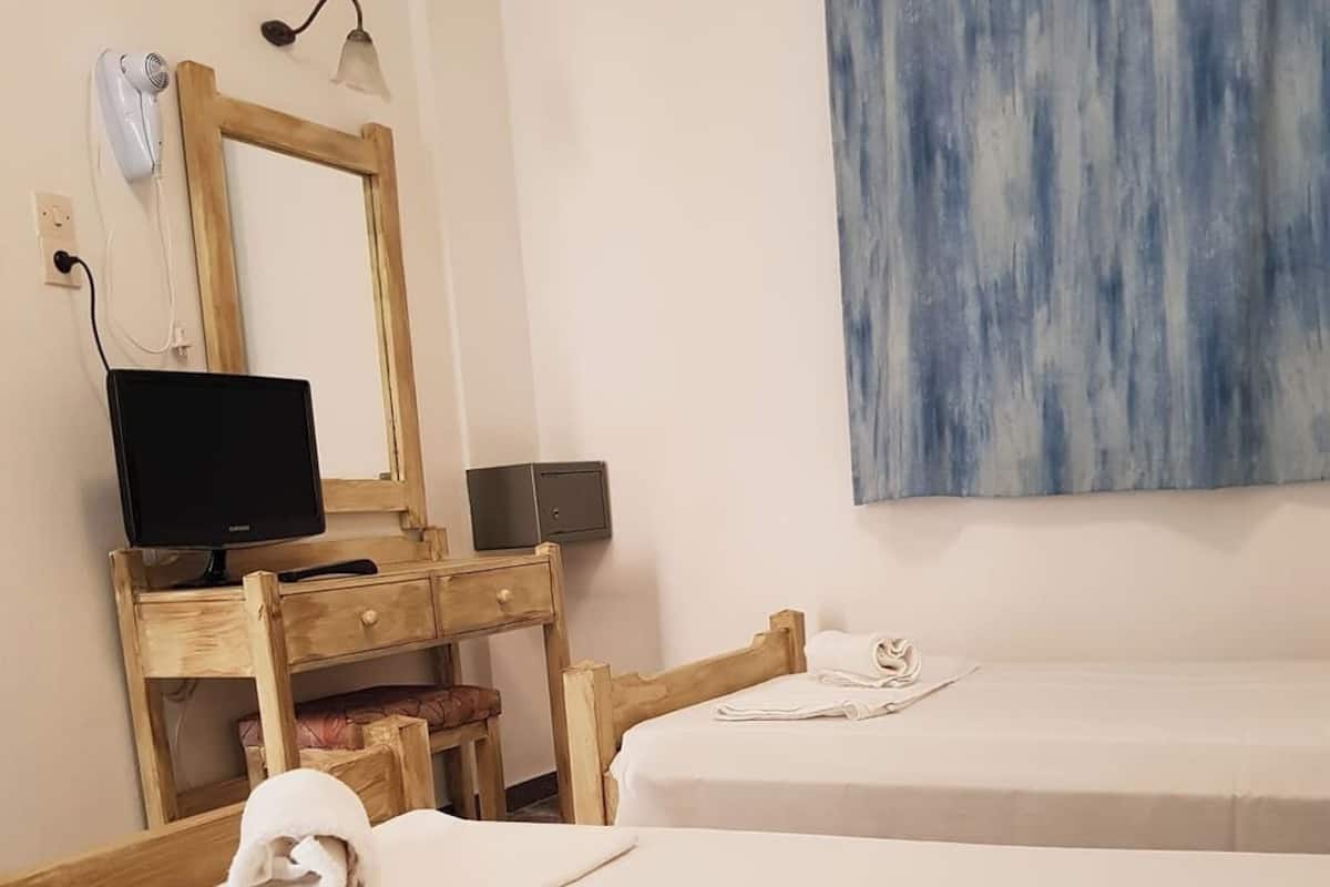 A hotel room with two beds, a wooden desk with a computer, a hairdryer, and a wall-mounted lamp.