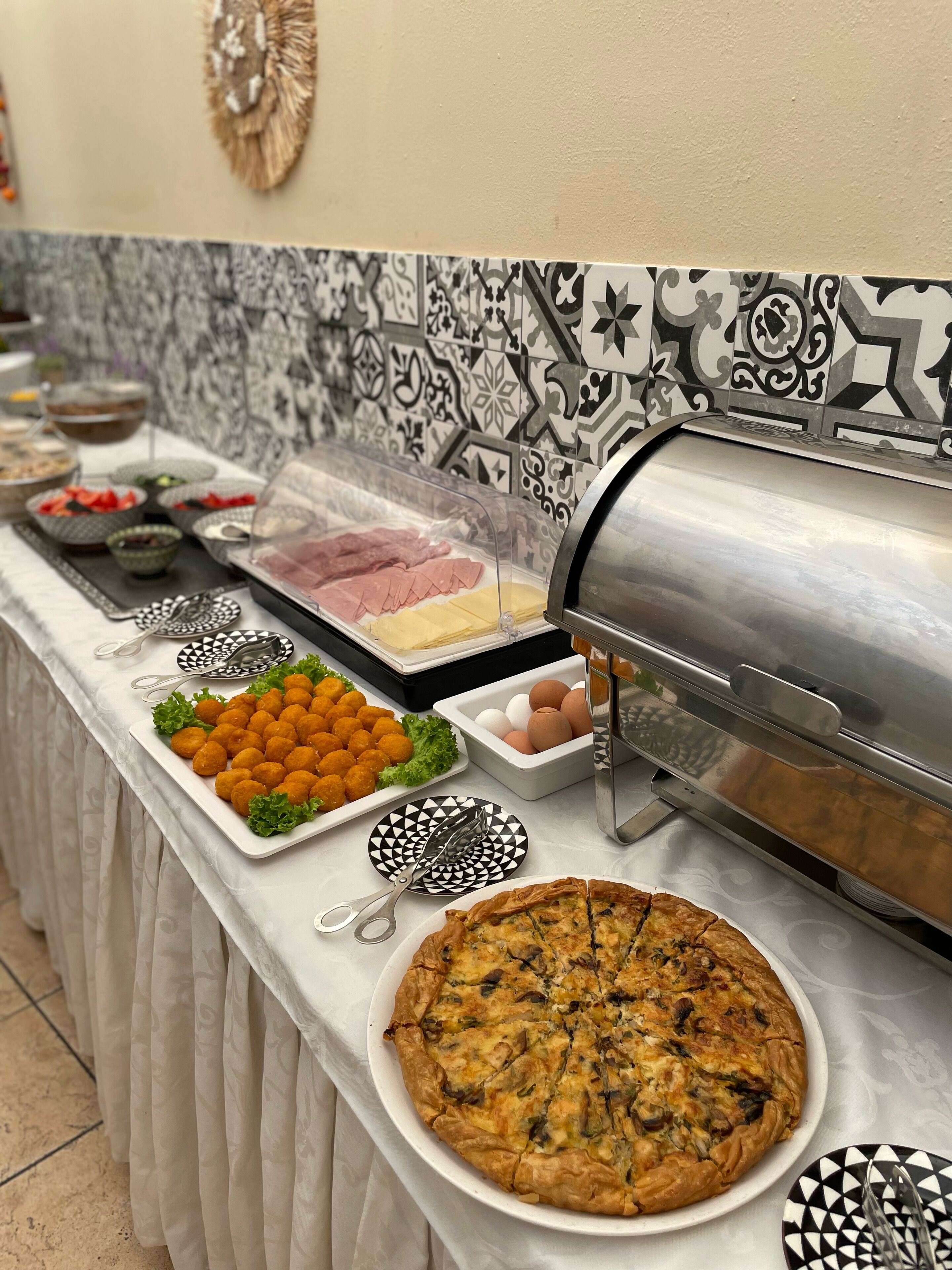 Une table de buffet proposant divers plats, notamment une quiche, des croquettes et des tranches de viande, ainsi que des condiments et des ustensiles de service.