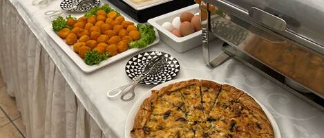 A buffet table with various food items, including a quiche, croquettes, and meat slices, along with condiments and serving utensils.