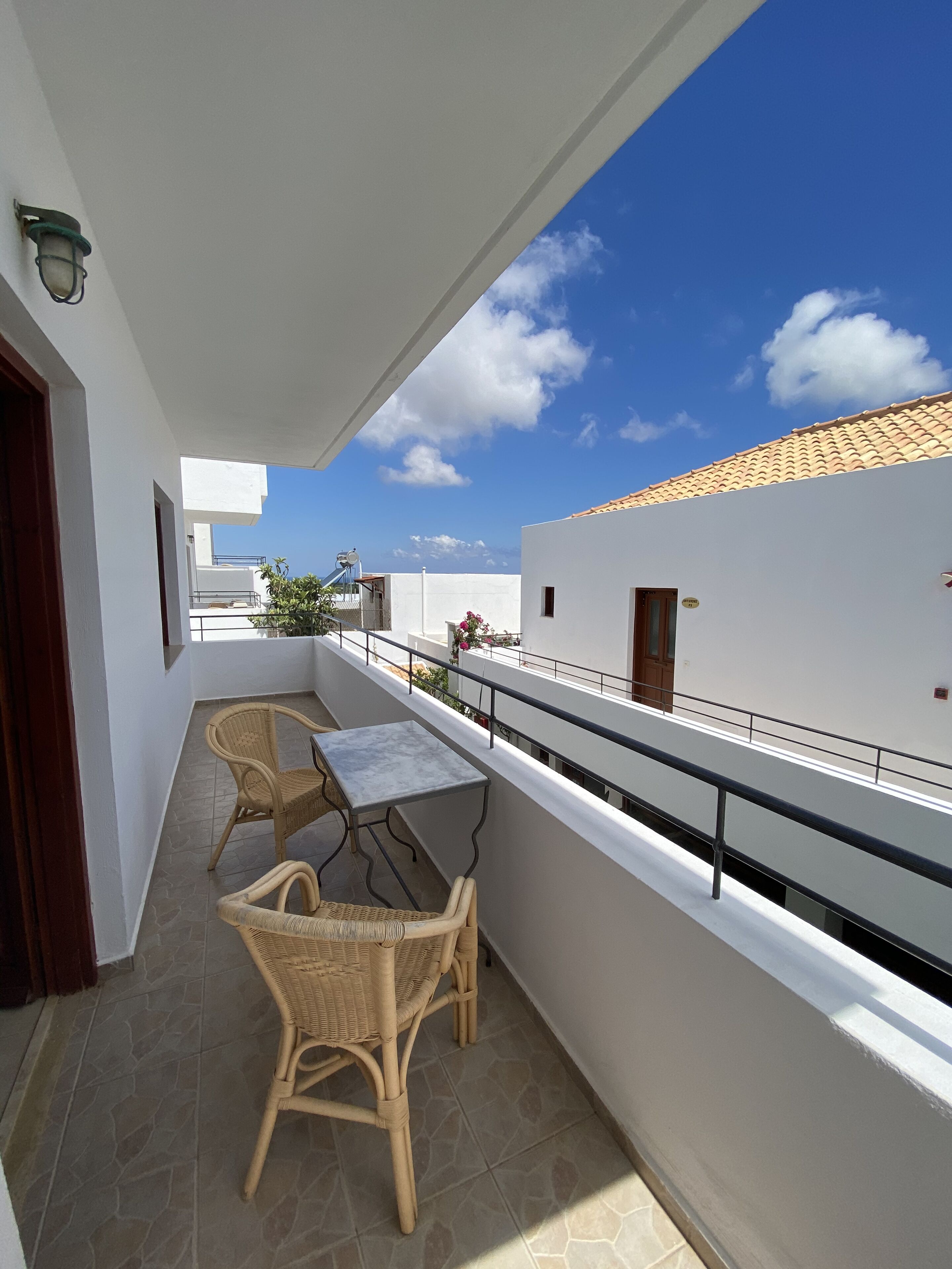 A balcony with wicker chairs and a table, white walls, and a clear blue sky.