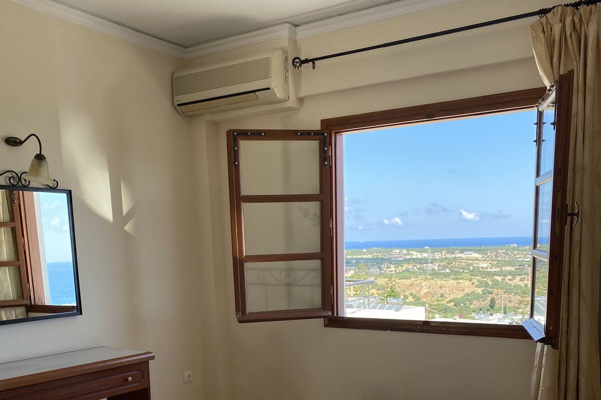 A hotel room with a bed, a desk, a mirror, and a window with a view of the landscape.