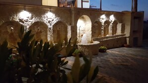 A stone courtyard with arches and a fountain, illuminated by wall-mounted lights. - Amazones Village Suites (Hersonissos)