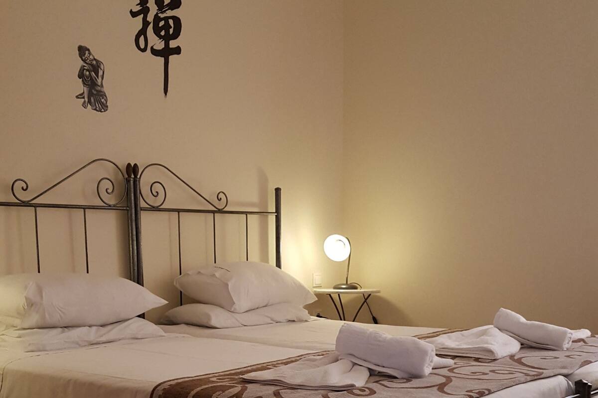 A neatly made bed with white linens and a brown decorative throw, a bedside table with a lamp, and a wall with a decorative item.