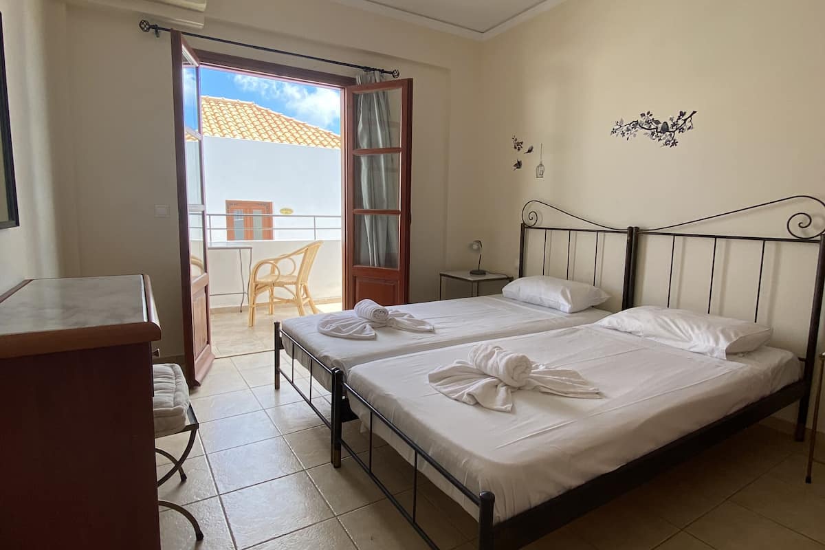 A bedroom with two beds, a desk, and a balcony with a chair.