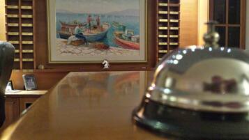 A wooden table with a glass dome centerpiece, a framed painting of boats on a pier, and a wooden shelf with labeled compartments.