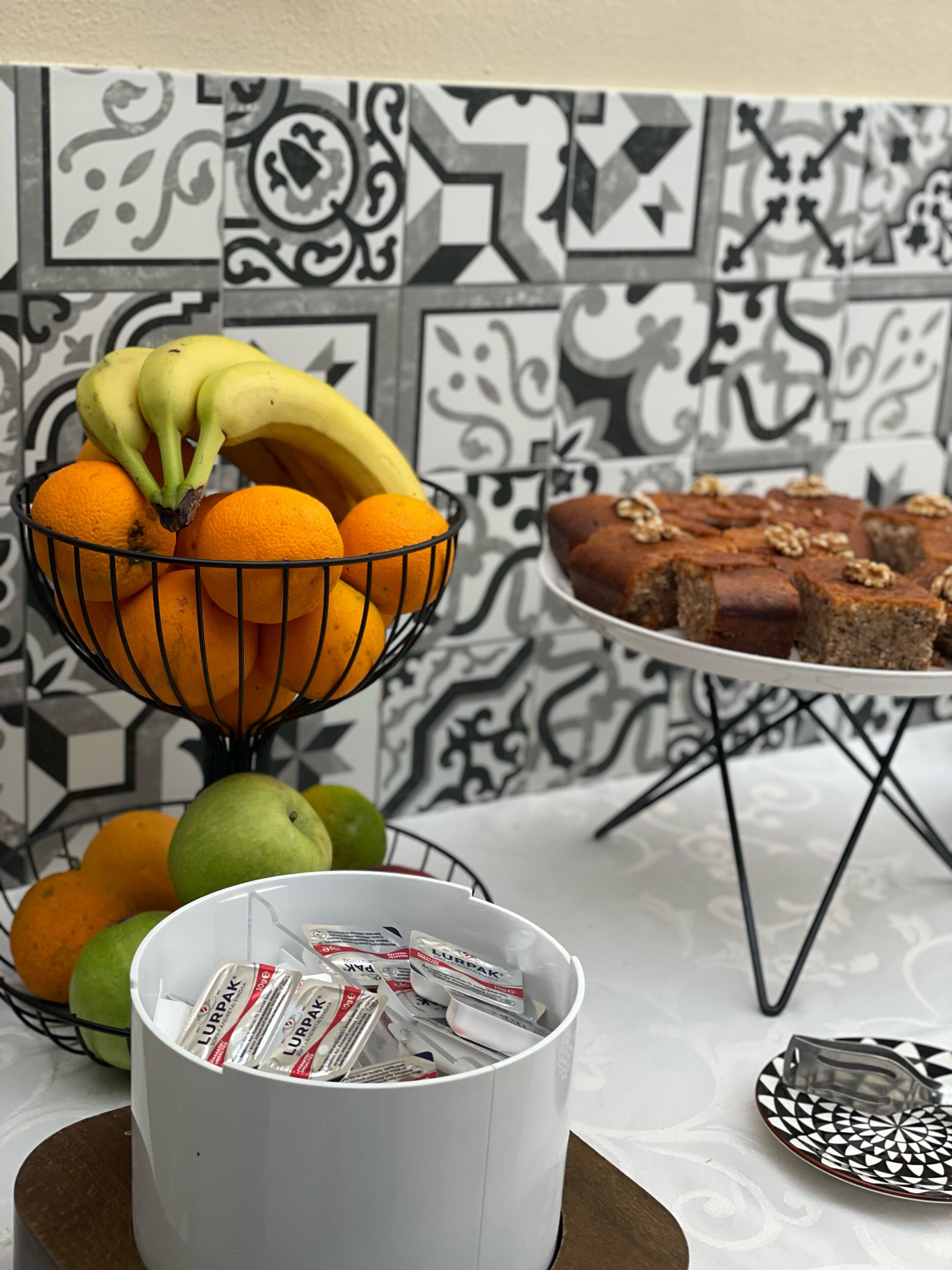 Une table avec un saladier rempli de bananes et d’oranges, une assiette de brownies et une tasse contenant des céréales Lurpak.