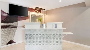 Un comptoir d’accueil au design moderne, un téléviseur à écran plat fixé au-dessus, et un mur décoratif sur le côté gauche.