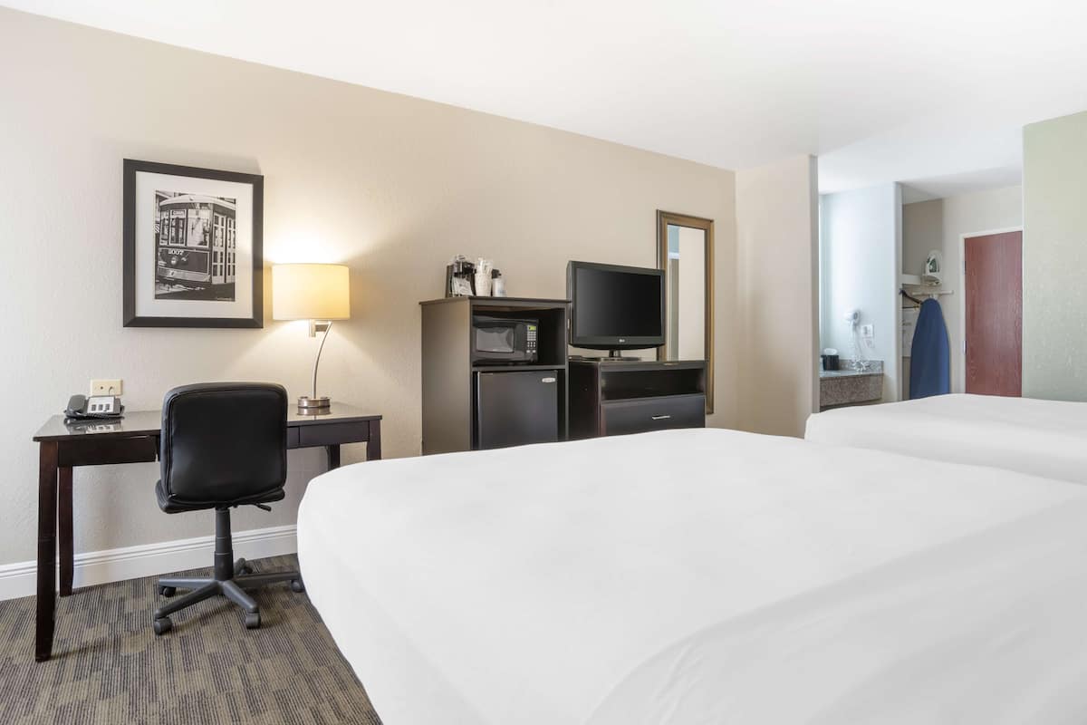A hotel room with a bed, a desk with a chair, a television, a microwave, and a framed picture on the wall.