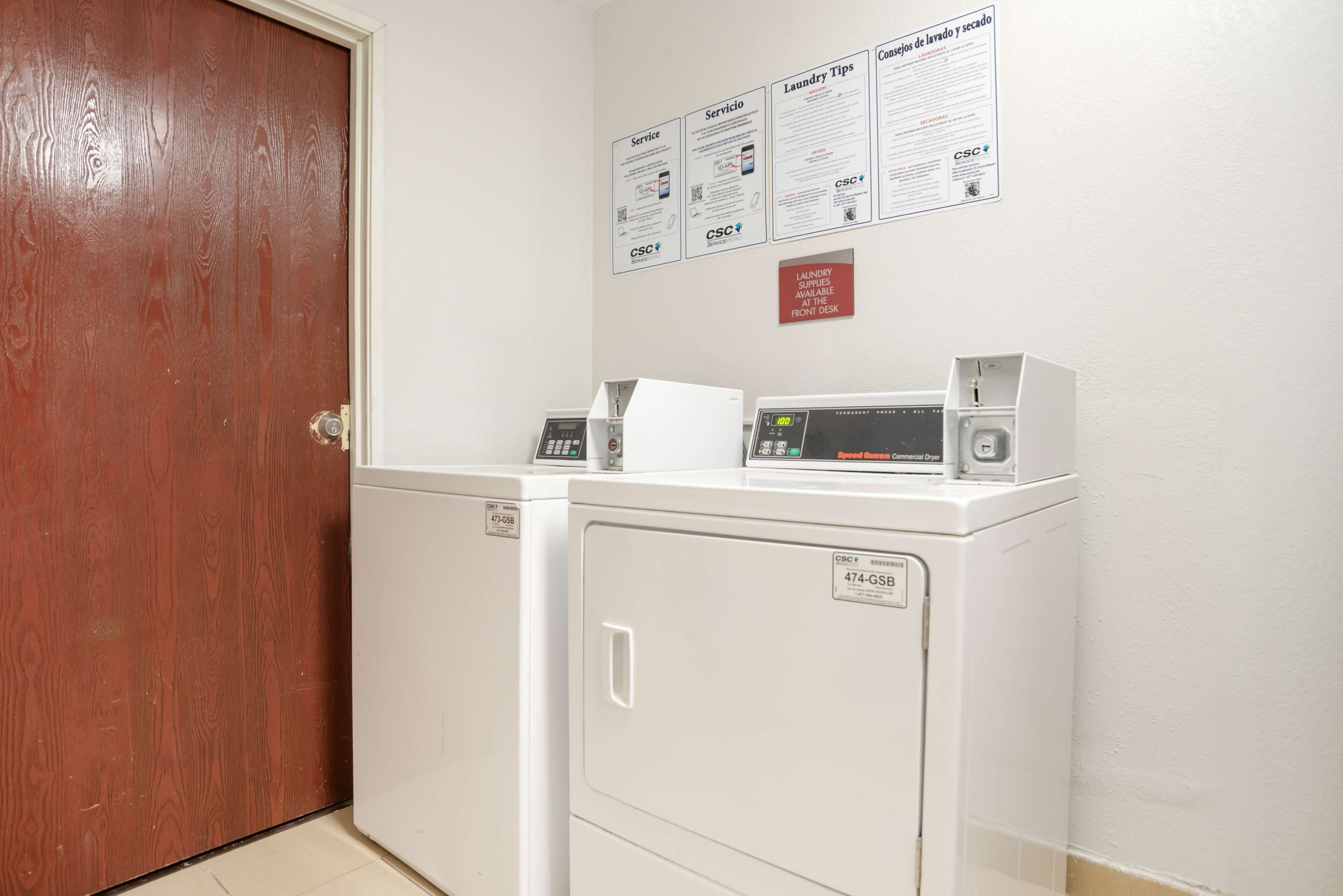 Un área de lavandería con dos lavadoras blancas, una puerta de madera y una pared con carteles informativos.