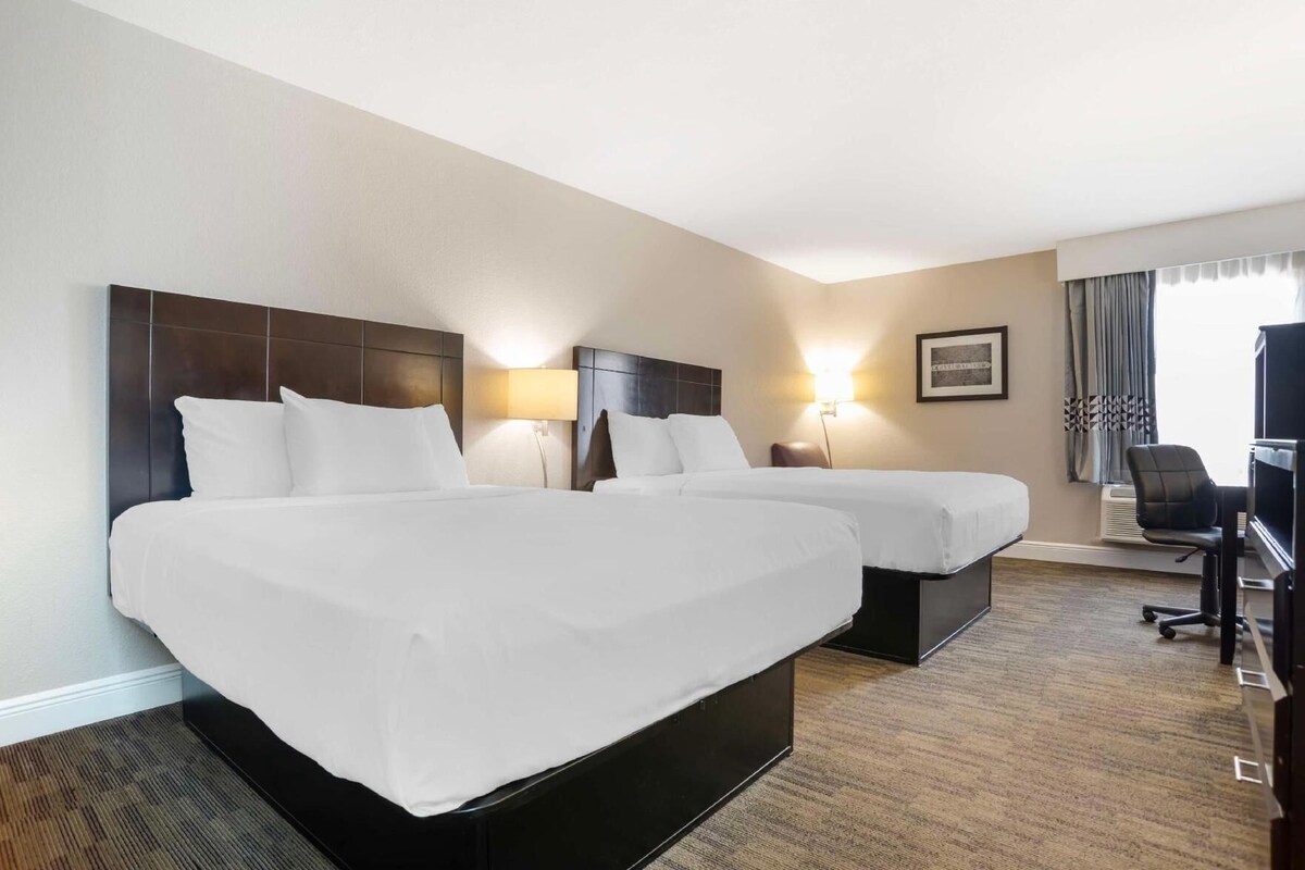 A hotel room with two beds, a desk, a chair, and a television.
