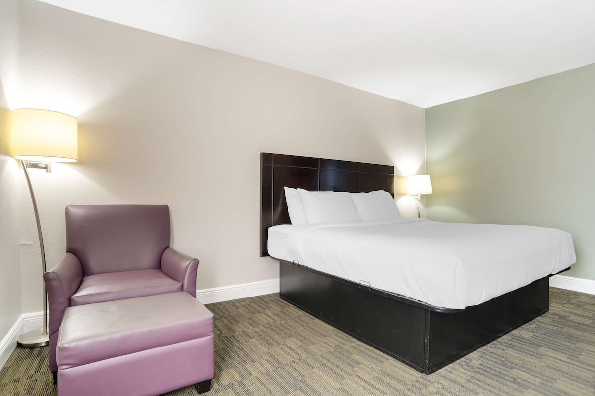 A hotel room with a bed, a chair, and two wall-mounted lamps.