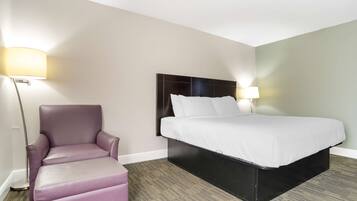 Una habitación de hotel con una cama, una silla y dos lámparas fijadas a la pared.