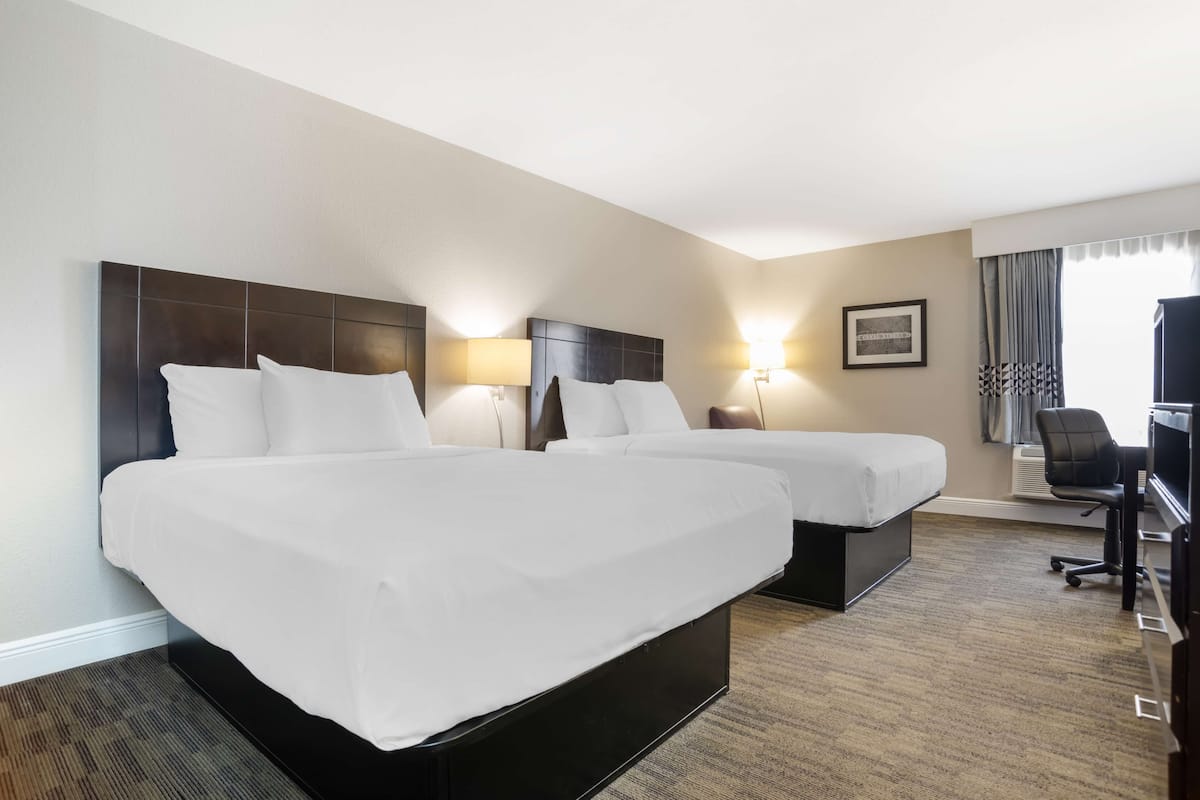 A hotel room with two beds, a desk, and a chair.