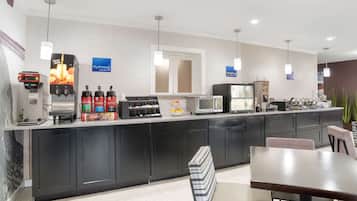 Una cocina de hotel moderna con estación de café, microondas y refrigerador.