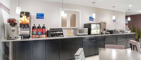 A modern hotel kitchen with a coffee station, microwave, and refrigerator.