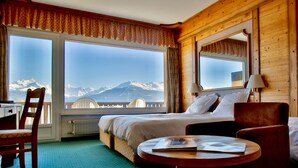 Een hotelkamer met een bed, een stoel, een tafel en een groot raam met uitzicht op bergen.