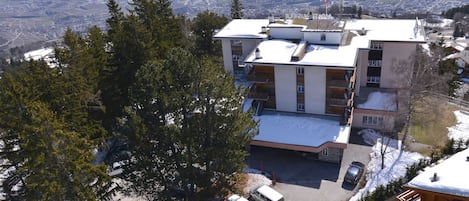 A multi-story hotel with a parking area, surrounded by snow-covered landscape and trees.