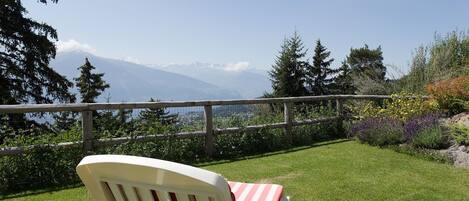 Une chaise dotée d’un coussin à rayures, placée de manière à offrir une vue panoramique sur un paysage comprenant des montagnes et un lac.