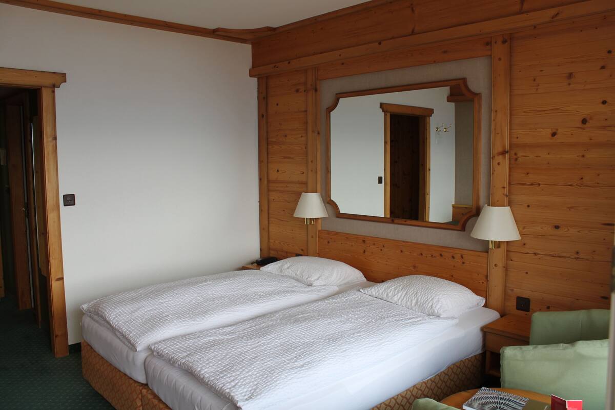 Ein Doppelbett mit weißer Bettwäsche, einem Holz-Kopfteil, zwei Nachttischlampen und einem Spiegel über dem Bett.